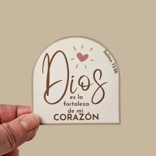 Sticker with Spanish text 'Dios es la fortaleza de mi corazón' held by a hand on a beige background