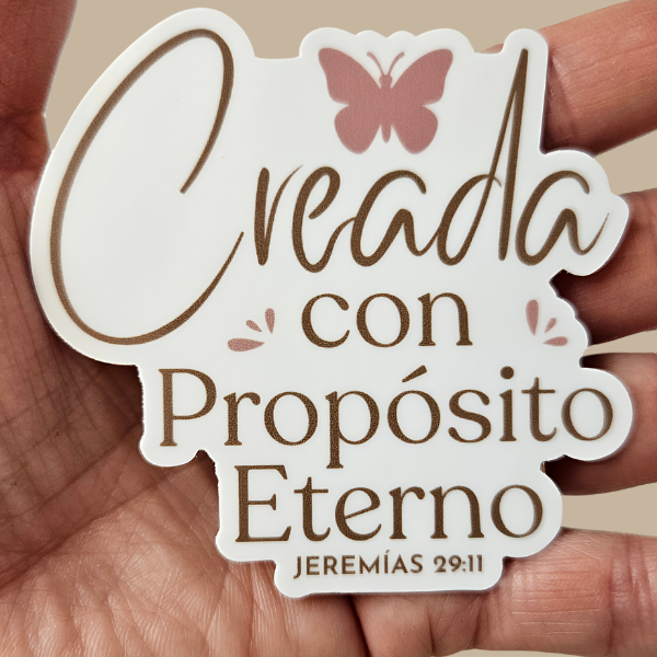 Hand holding a decorative sticker Creada con propósito eterno Jeremías 29:11 and a butterfly design.